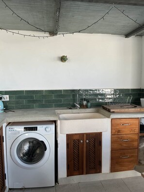A compact kitchen with a built-in washing machine, a sink, and wooden cabinets. - Casa Blanca | Lecrin Valley, Granada (Acequias)