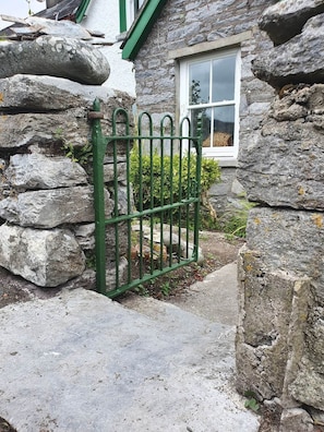 Una casa de piedra con una verja verde de metal y una ventana con una cesta.