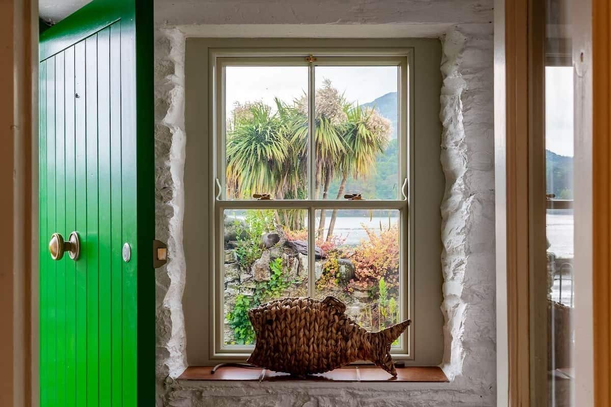 A room with a green door, a window with a view of palm trees and a mountain, and a woven basket on the windowsill.