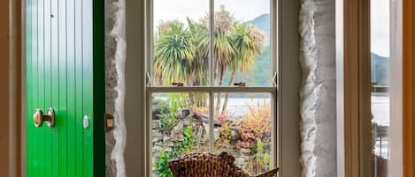 A room with a green door, a window with a view of palm trees and a mountain, and a woven basket on the windowsill.