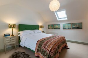 A bedroom with a green headboard, a skylight, a bed with white linens, a patterned throw blanket, and three sailboat paintings on the wall. - Kenmare Pier Cottage 
Cosy sea side home . (Kenmare)