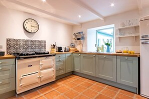 A kitchen with a stove, oven, and cabinets, a clock on the wall, and a window with a view. - Kenmare Pier Cottage 
Cosy sea side home . (Kenmare)