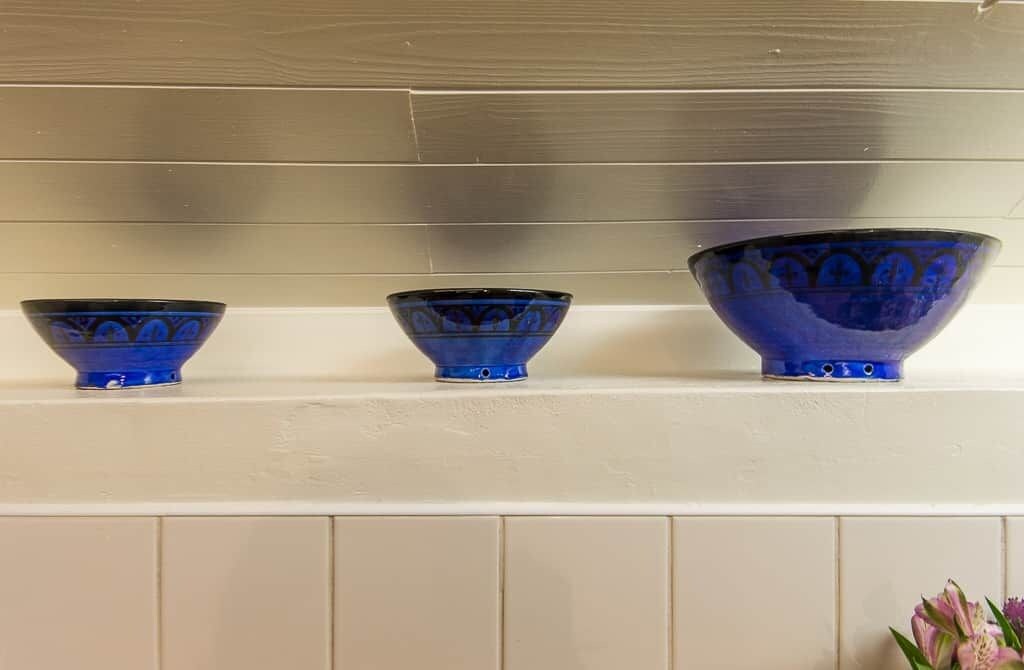 Tre blå keramikskålar står på en vit hylla framför en vägg av metall.