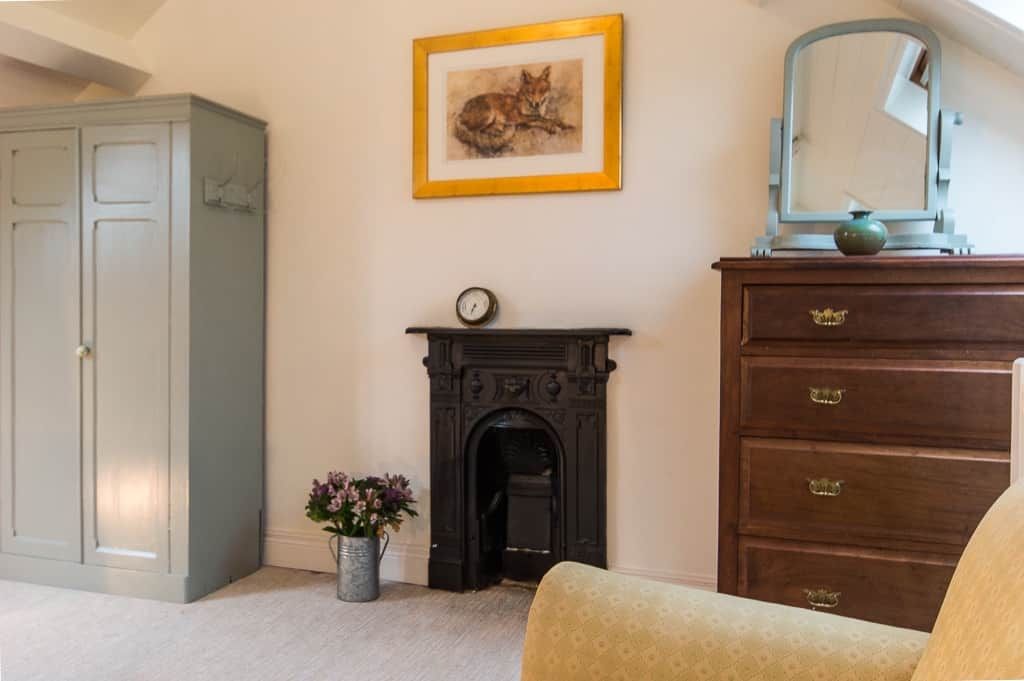 A room with a fireplace, a dresser, a mirror, a framed picture, and a cabinet.