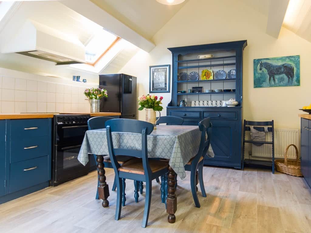 A kitchen with a dining table, chairs, a blue cabinet, and a painting on the wall.
