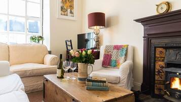 A cozy living room with a fireplace, a sofa, a coffee table with books and glasses, and a lamp.
