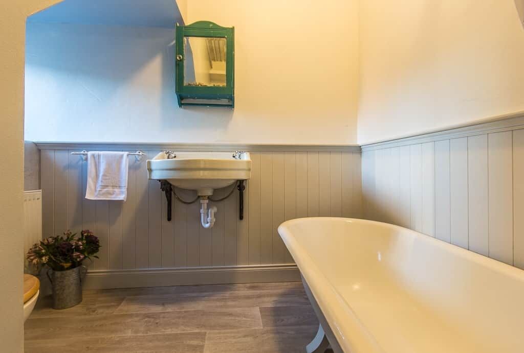 A bathroom with a white bathtub, a sink with a green mirror, and a potted plant.
