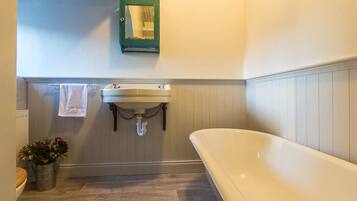 A bathroom with a white bathtub, a sink with a green mirror, and a potted plant.