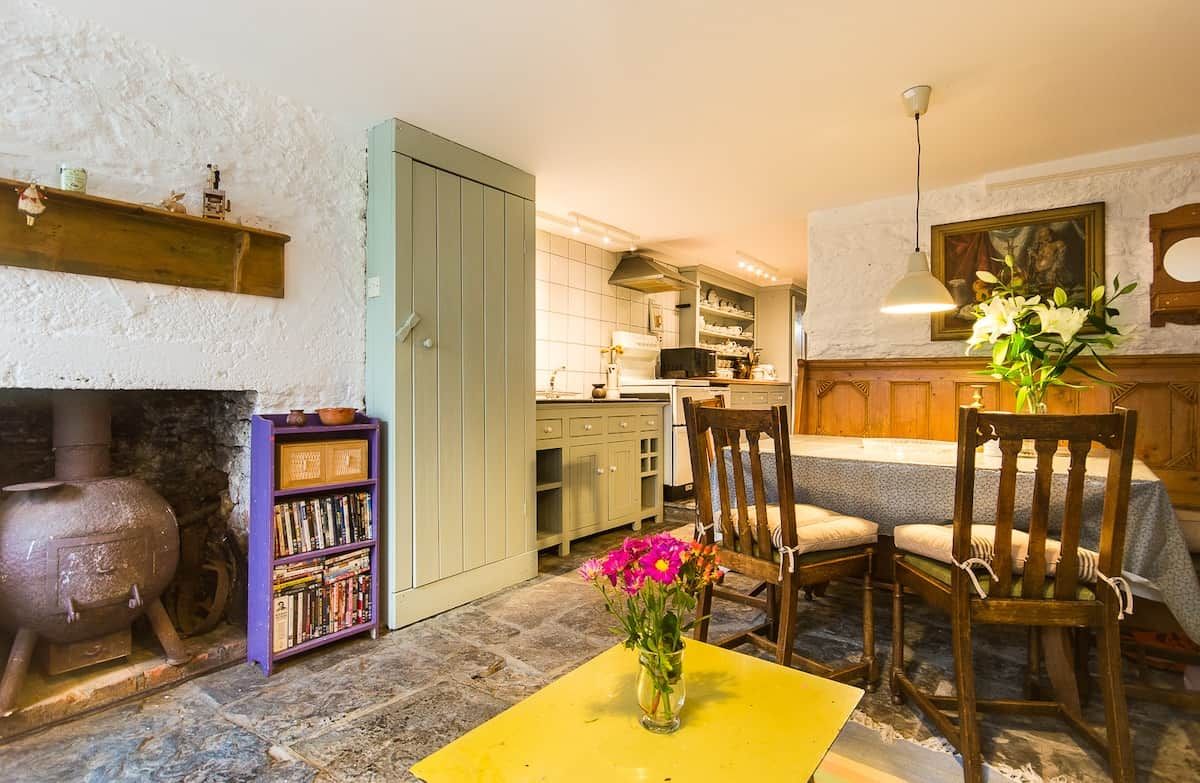 Una habitación acogedora con chimenea, una estantería, una mesa de comedor con sillas y una cocina al fondo.