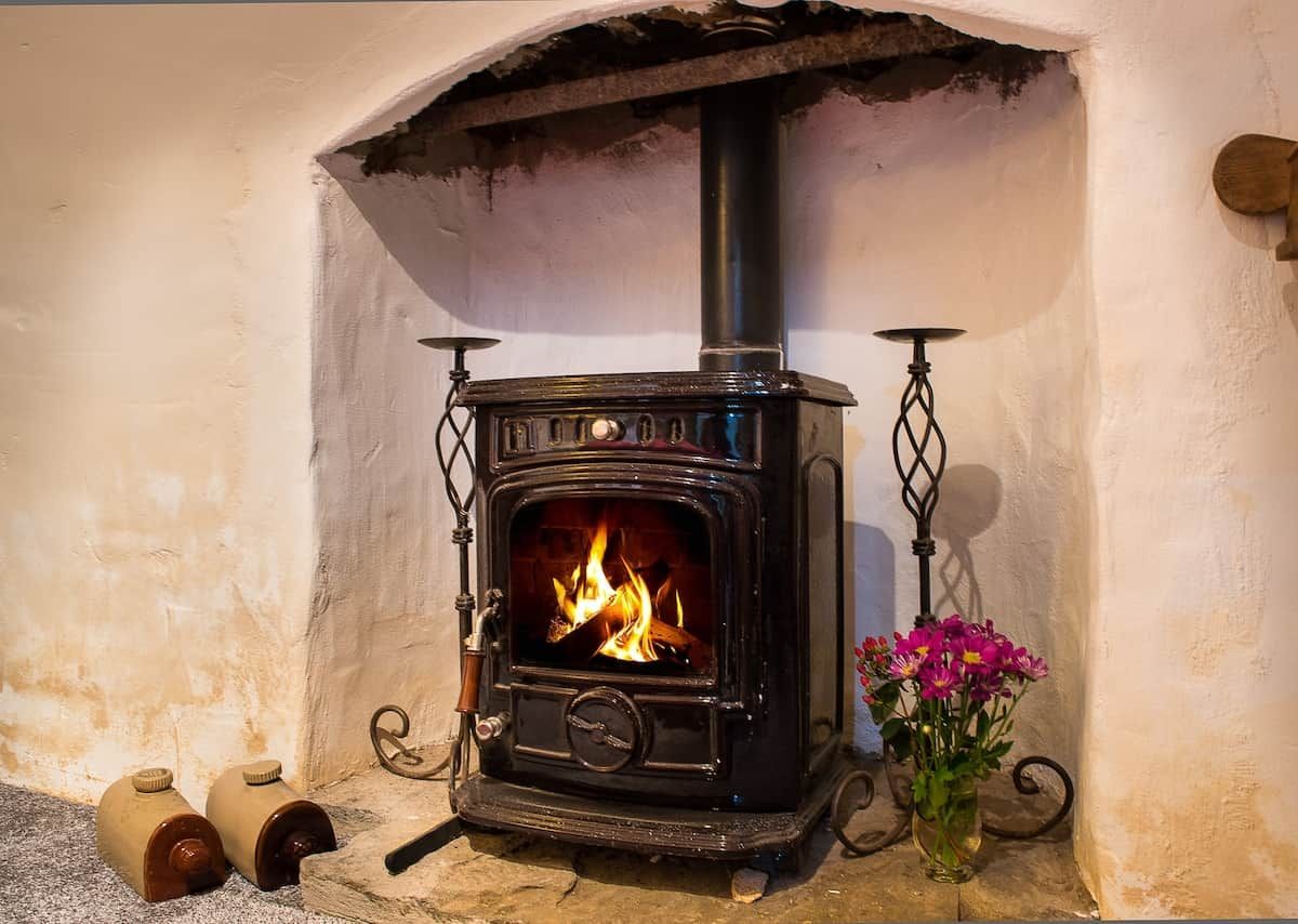 A black wood-burning stove with a visible fire, a flower vase, and two wooden containers on the floor.