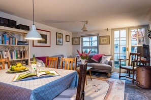 A cozy living room with a dining area, bookshelves, and a large window. - Cleo Gallery basement Apartment (Kenmare)