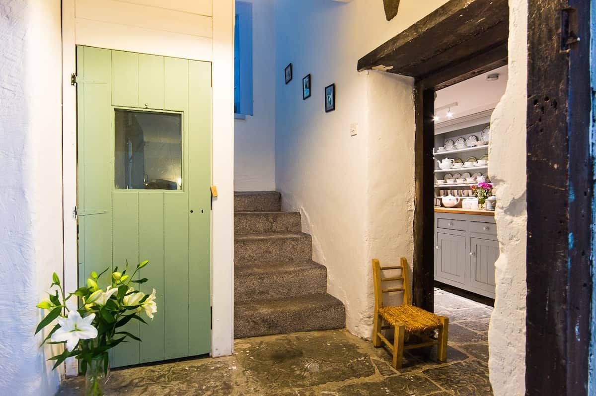 A staircase leading to a room with a green door, a chair, and a vase with flowers.