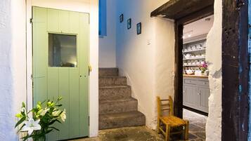 A staircase leading to a room with a green door, a chair, and a vase with flowers.