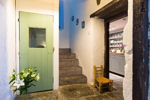 A staircase leading to a room with a green door, a chair, and a vase with flowers.