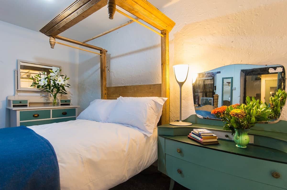 A bedroom with a bed, bedside table, lamp, mirror, and a dresser.