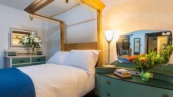 A bedroom with a bed, bedside table, lamp, mirror, and a dresser.