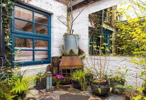 A rustic stone pathway leading to a white building with a blue window and a metal water tank. - Cleo Gallery basement Apartment (Kenmare)