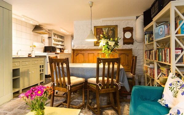 A cozy living room with a dining area, a bookshelf, and a kitchen in the background.