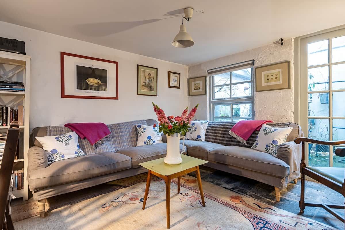 Una sala de estar con un sofá, una mesa con un florero y cuadros en la pared.