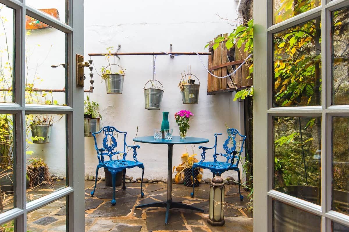 Eine Terrasse mit Tisch und Stühlen, umgeben von Kübelpflanzen und hängenden Pflanzgefäßen.