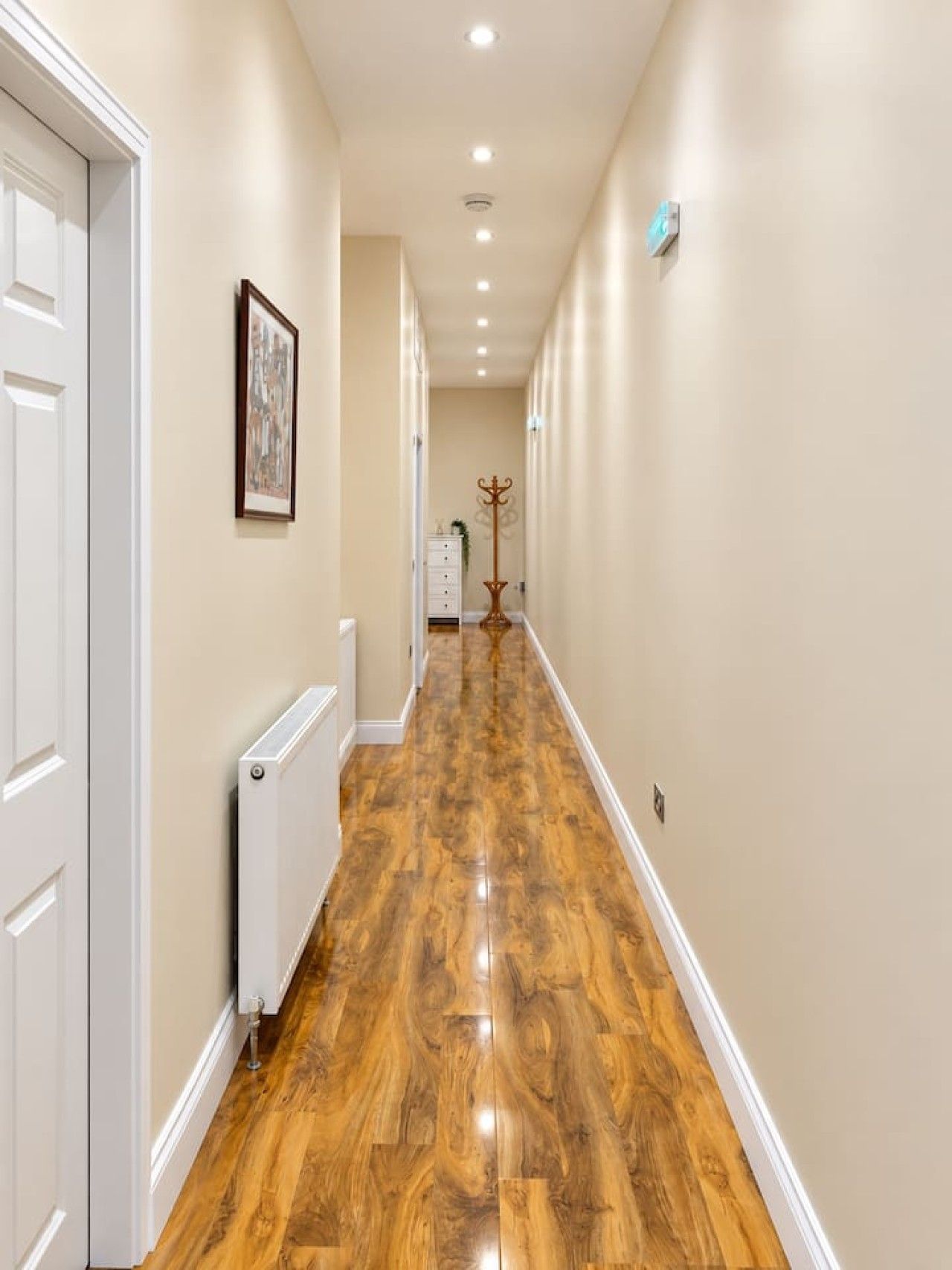 A hallway with wooden flooring, white walls, and a radiator.