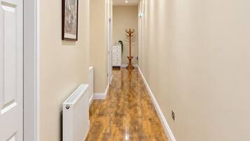 A hallway with wooden flooring, white walls, and a radiator.