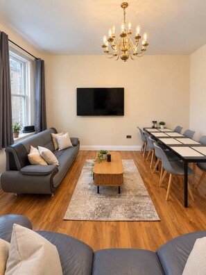 A modern living room with a sofa, coffee table, TV, and dining area.