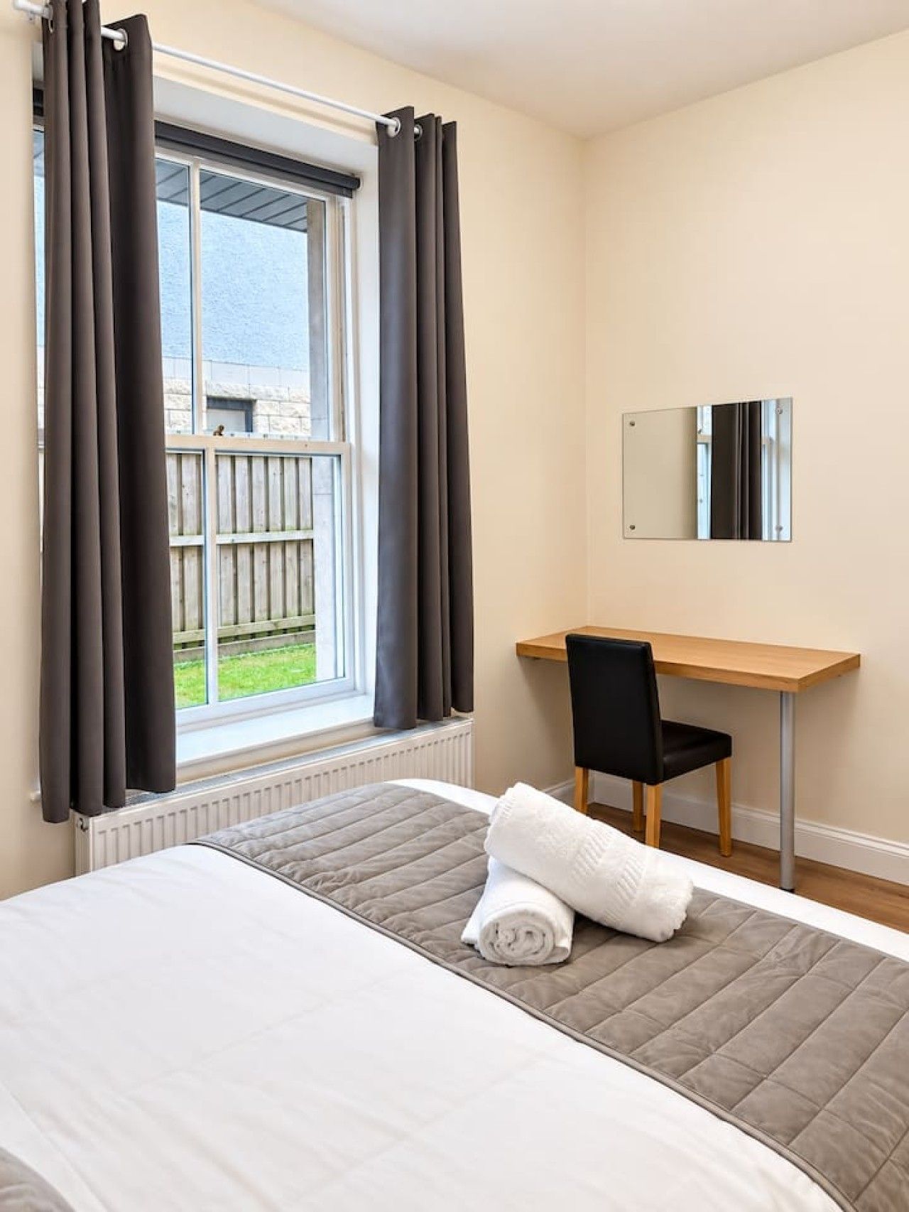 Een hotelkamer met een bed, een bureau, een stoel, een raam met gordijnen en uitzicht op buiten.