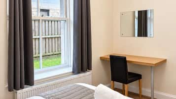 Een hotelkamer met een bed, een bureau, een stoel, een raam met gordijnen en uitzicht op buiten.