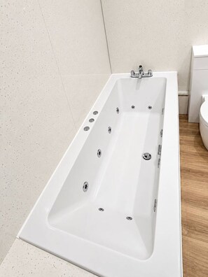 A modern bathroom with a white bathtub, a toilet, and a shower area. - Stylish Modern Apartment (Edinburgh)