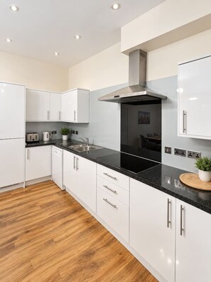 A modern kitchen with white cabinets, a black countertop, and a stainless steel range hood.