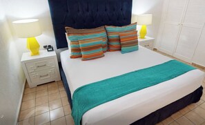 A hotel room with a bed, striped pillows, a teal throw, two bedside lamps, and a wardrobe.