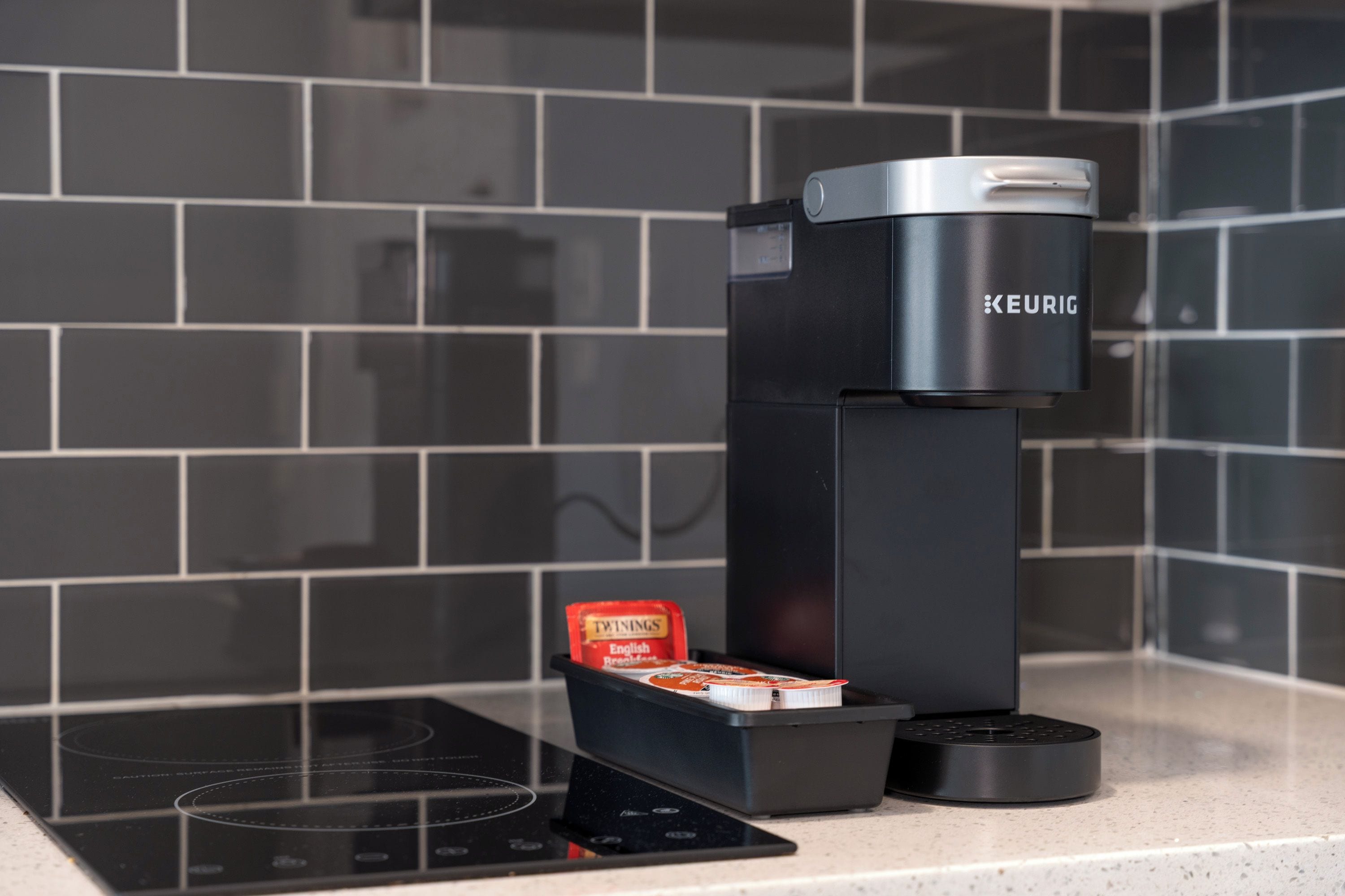 Ett modernt kök med en svart kaffemaskin, en vattenkokare och ett ställ för kaffekapslar på bänkskivan.