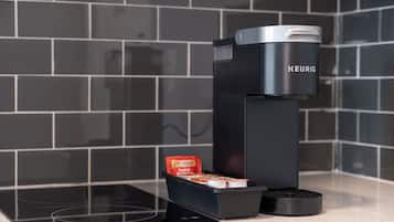Ett modernt kök med en svart kaffemaskin, en vattenkokare och ett ställ för kaffekapslar på bänkskivan.