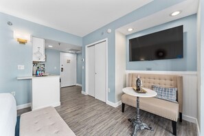 Ett hotellrum med en sittgrupp, en tv som är monterad på väggen och ett litet bord med en flaska och ett glas.
