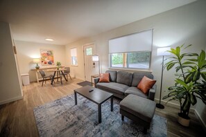A living room with a sofa, ottoman, coffee table, and a dining area with chairs and a table. - Stay Roanoke | Cozy 1BR Near Hospital, Downtown (Roanoke)