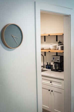 A kitchen with a wall clock, shelves with dishes, and a coffee machine. - Stay Roanoke | Cozy 1BR Near Hospital, Downtown (Roanoke)
