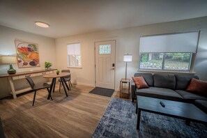 A modern living room with a sofa, coffee table, and a dining area with chairs and a table. - Stay Roanoke | Cozy 1BR Near Hospital, Downtown (Roanoke)