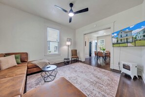 A spacious living room with a brown leather sofa, a round coffee table, and a ceiling fan. - Stay Roanoke | Patterson Pad | Roomy 3BR in Town (Roanoke)