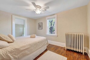 Ein Schlafzimmer mit Bett, Deckenventilator, Fenster und Heizkörper.