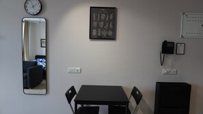 Ein Zimmer mit Esstisch, Stühlen, einem Spiegel, einer gerahmten Pflanzenillustration, einer Uhr und einem Telefon.