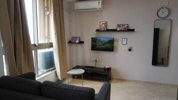 Een woonkamer met een bank, een bijzettafeltje, een televisie en een aan de muur hangend schilderij.