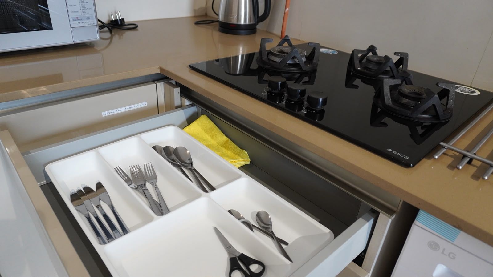 A kitchen with a gas stove, a microwave, and a drawer with utensils.