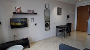 Una habitación con televisión de pantalla plana, lavadora, un reloj y una puerta.