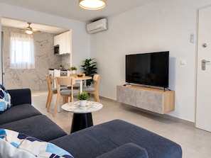 A modern living room with a sofa, a television, a dining area with a table and chairs, and a kitchen in the background. - Jardin del Mar House Torrevieja (Torrevieja)