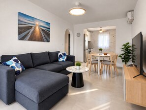 A modern living room with a sofa, a coffee table, a TV, and a dining area with chairs and a table. - Jardin del Mar House Torrevieja (Torrevieja)