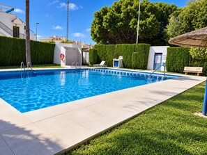 A rectangular swimming pool with a clear blue water surface, surrounded by a tiled deck and a well-maintained lawn. - Jardin del Mar House Torrevieja (Torrevieja)