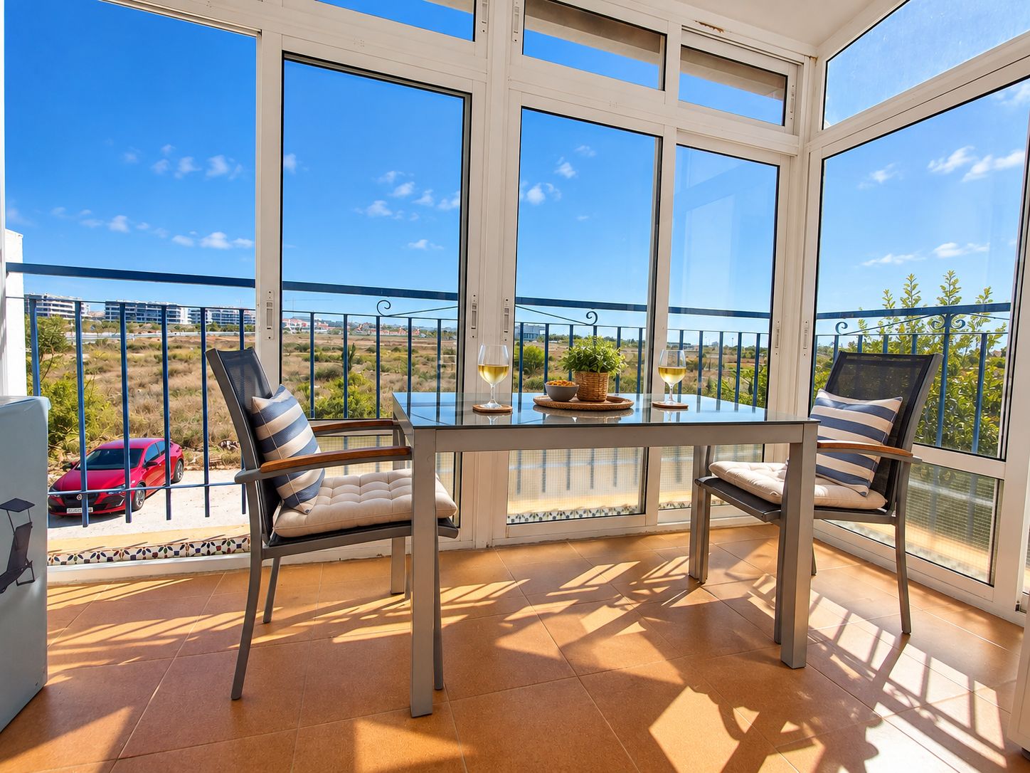 A sunlit balcony with a table, chairs, and a view of the countryside.