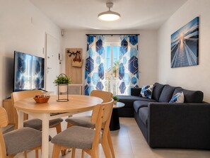 A modern living room with a wooden dining table, grey upholstered chairs, a dark grey sofa, and a large flat-screen TV. - Jardin del Mar House Torrevieja (Torrevieja)