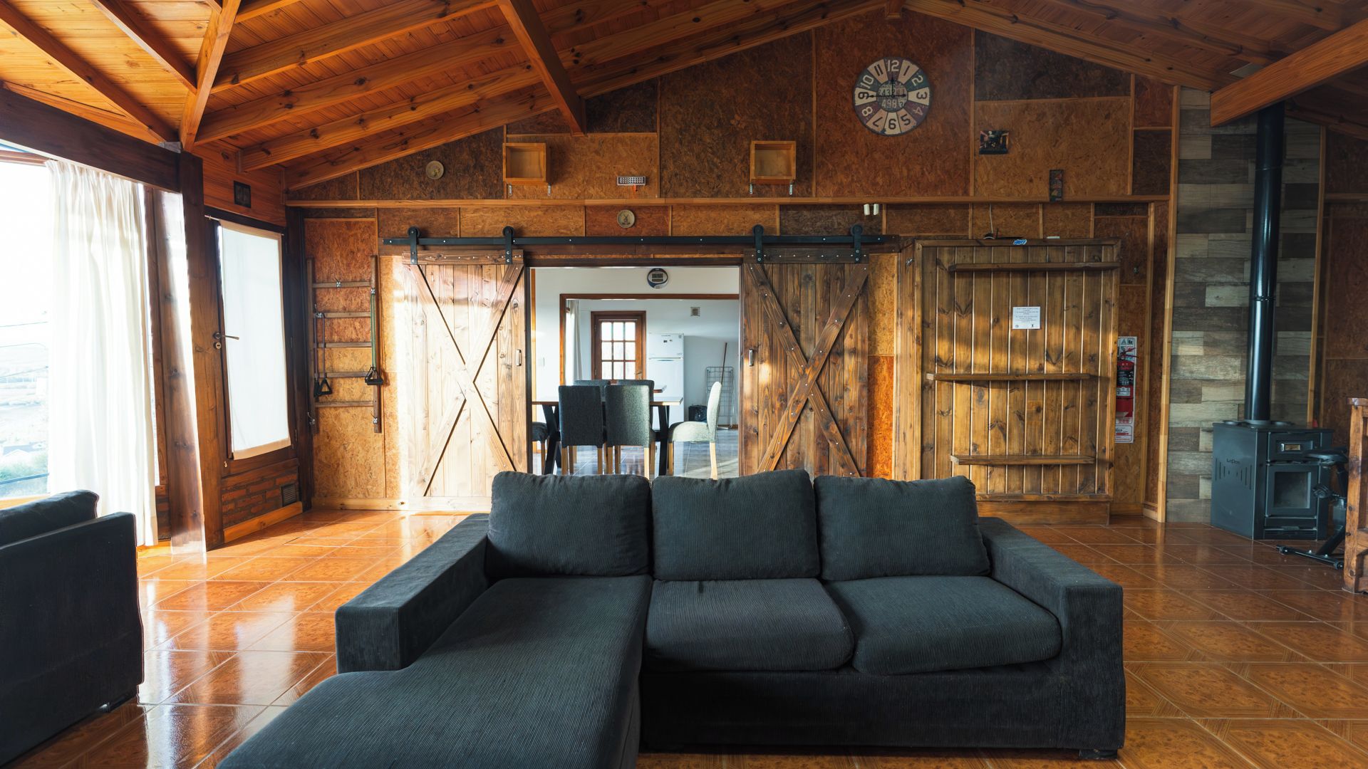 A rustic interior with a large sectional sofa, wooden walls, a clock, and a fireplace.